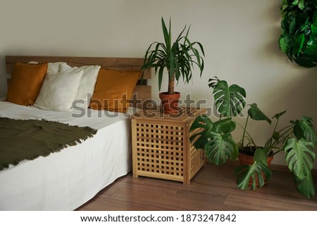 bedroom in soft light colors. big comfortable double bed in elegant classic bedroom. many green plants. natural wooden materials. Royalty-Free Stock Photo #1873247842