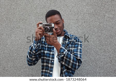 Handsome young African-American man in casual clothes feeling confident, squinting, taking picture on vintage film camera. Copy space for advertising or promotion. People, lifestyle and photo concept.