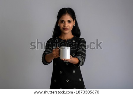pretty young girl with a cup of tea or coffee posing on grey background