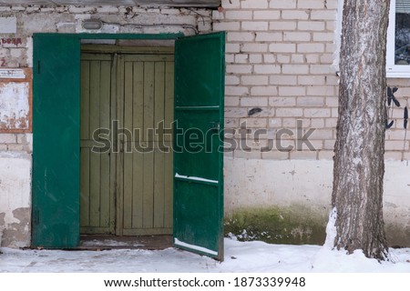 picture of the public entrance of the typical Russian ghetto. Soviet Union stylization in 2020. Khrushchev building Facade Opened door. Winter image.
