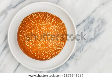 Freshly baked homemade Sesame bun for hamburger or cheeseburger close-up in a white plate on a marble background. Selective focus, top view and copy space
