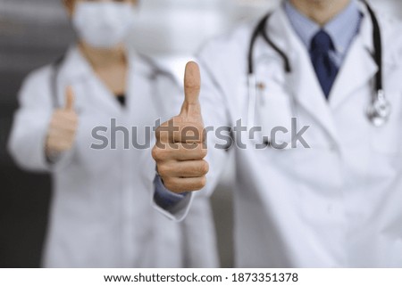 Unknown man-doctor and woman standing straight as a team and showing Ok sign with thumbs up in modern clinic. Medicine concept during Coronavirus pandemic. Covid 2019