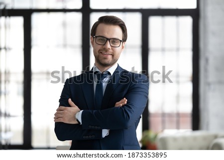Head shot portrait smiling confident businessman wearing suit and glasses looking at camera, profile picture successful executive company owner with arms crossed standing posing in modern office