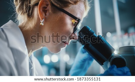 In Bright Medical Science Laboratory: Beautiful Microbiologist Wearing Glasses Looks Under Microscope Analyzing Sample. Brilliant Scientist, Doctor, working with High-Tech Equipment. Close-up Shot Royalty-Free Stock Photo #1873355131