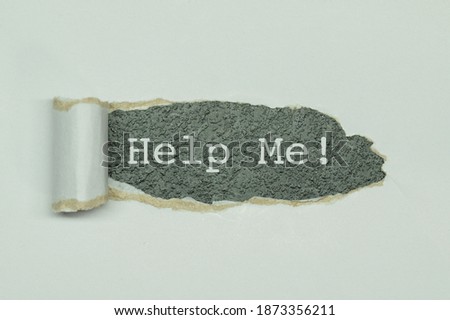 Text Help me appearing behind torn white paper. top view of open white paper and the message Help me written behind on dark background
