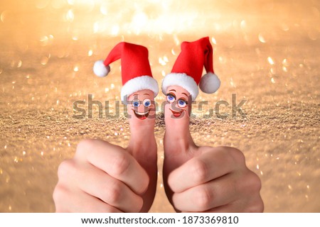 Two hands are holding thumbs up. Santa Claus hats are put on the fingers and funny cartoon faces are drawn. Great mood in the new year.