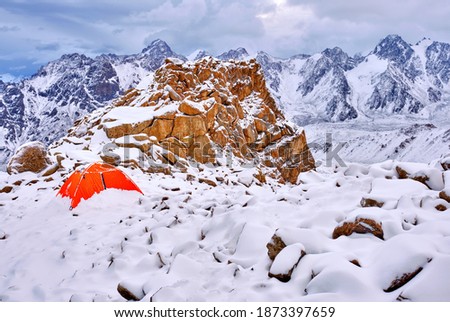 Tent next to the expressive rock is covered with a layer of snow after an overnight snowfall in the highlands; mountains after a snowfall in the morning, travel and tourism concept