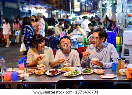Asian family enjoy eating food on street food restaurant with crowd of people at Yaowarat road, Bangkok Royalty-Free Stock Photo #1873406731