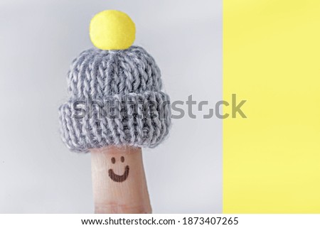 Funny finger in knitted warm small hat, winter season concept. Duotone colored of pantone colors 2021 - Illuminating Yellow and Ultimate Gray