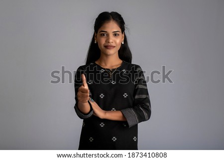 Young smiling girl showing ok sign or thumbs up on a grey background