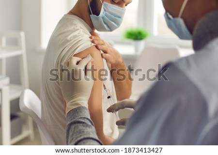 Immunization and disease prevention concept. Doctor giving antivirus injection to young man. Close-up patient in medical face mask getting flu or Covid-19 antiviral vaccine during vaccination campaign Royalty-Free Stock Photo #1873413427