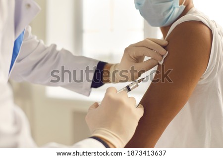 Doctor in medical gloves giving Covid-19, AIDS or flu antivirus vaccine shot to African-American patient. Close-up of hands holding syringe and cleaning skin on upper arm before antiviral injection Royalty-Free Stock Photo #1873413637