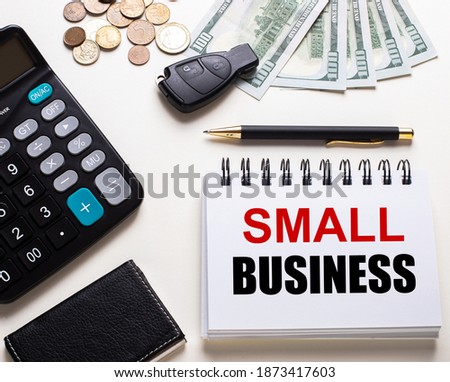 On a white table is a calculator, car key, cash, a pen and a notebook with the inscription SMALL BUSINESS
