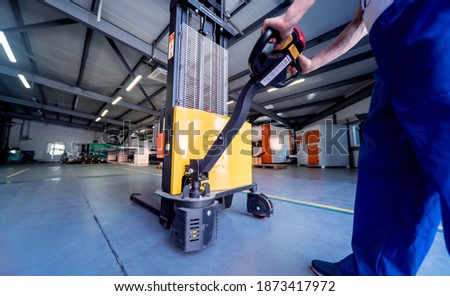 A worker in a warehouse uses a hand pallet stacker to transport pallets. Royalty-Free Stock Photo #1873417972
