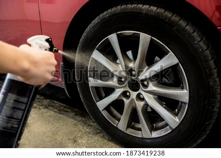 Service worker washing car wheell at a car wash.