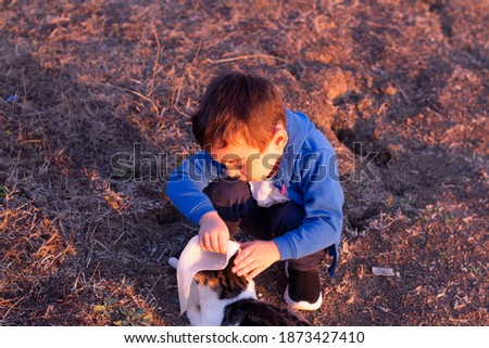 boy kid sitting outdoors on local road holding hand to black wild cat on rural road landscape. little child making friends with kitten in village. childhood happiness animals love
