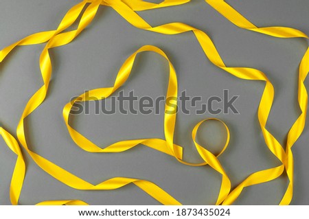 Yellow satin ribbon in the shape of a heart on a gray background.Trending colors 2021.Valentine's day.