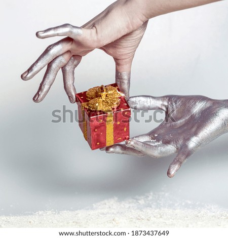 Close-up of female hands, painted in silver, holding a gift on a gray background.