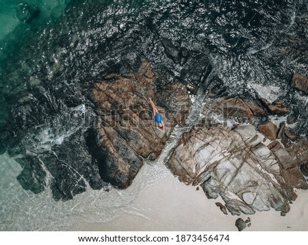 From above photo of a pretty young woman in a blue swimming suit lying on the rock in high tide. Summer vacation concept