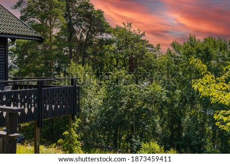 Gorgeous view of red cloudy sky during sunset and part facade of typical wooden Swedish house with wooden patio.  Beautiful nature backgrounds.