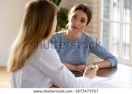 Young Caucasian female patient talk with nurse or GP at consultation in private hospital. Worried millennial woman consult speak with doctor in white medical uniform in clinic. Healthcare concept. Royalty-Free Stock Photo #1873471927