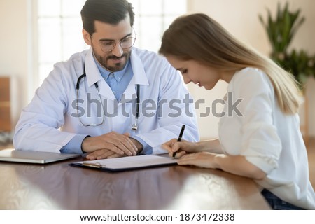 Female patient put signature on paperwork close deal with male GP or physician in private hospital. Woman client sign paper document mage health insurance agreement with man doctor in clinic.