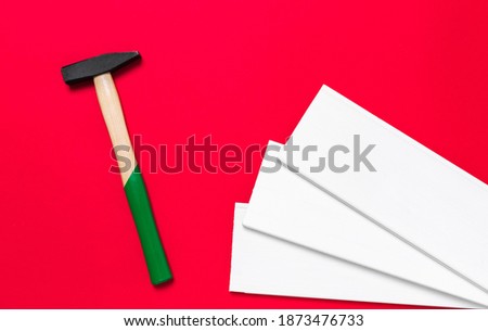 Hammer and white planks on a red background with place for text. Shop banner with construction tools, materials and instrument. New Year or Christmas holiday backdrop. Business card. Nobody.