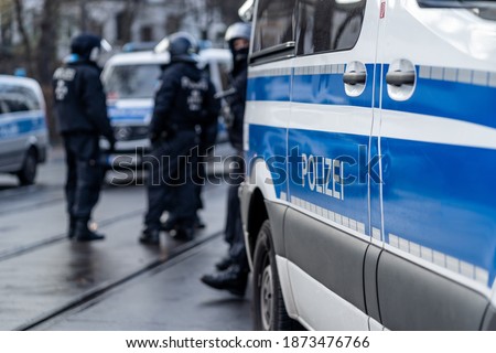 German police car from berlin is in the focus and in the blurry background are several riot police cops standing on the street and waiting for action on a demonstration.