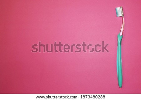new plastic turquoise toothbrush with white hairs on a pink background top view . oral hygiene