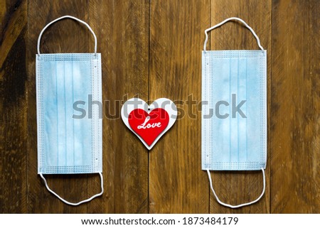 Two blue masks placed vertically and in the middle a red and white heart with the word love written in the center on a wooden background, seen from above