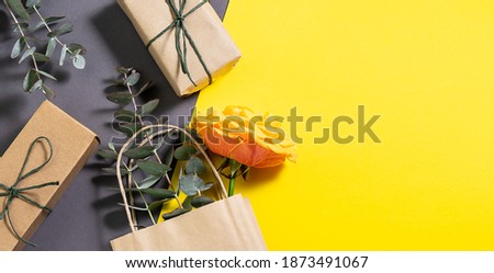 Creative composition with gift boxes and shopping bag from craft recycle paper, eucalyptus twigs and beautiful tea rose on trendy two tone background. Zero waste eco friendly holiday banner.
