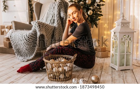 Beautiful cheerful happy young girl on the floor in pajamas with christmas toys near the new year tree at home