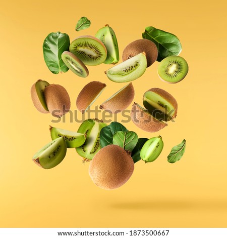 Fresh raw kiwi with leaves falling in the air isolated on yellow illuminating background. Food levitation concept. High resolution image