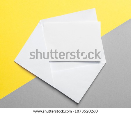 Blank paper card in envelope on yellow anf gray background. Mock up.