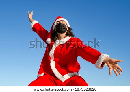 Picture of Excited Young Happy Santa Claus With Black Mask Opening Arms in Welcome Symbol with Blue Sky Background