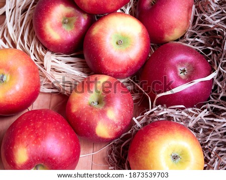 Bright red and yellow apples are stored in hay on a wooden surface         
