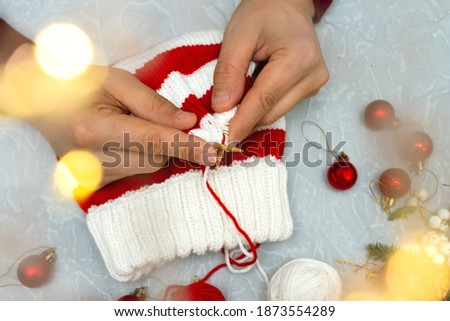 men's hands knit New Year's striped red and white hat, cap on gray background of Christmas balls and bokeh