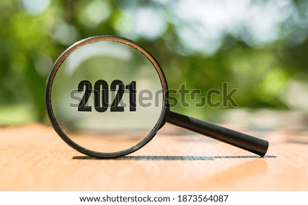 Magnifying glass with text 2021 on wooden table and green background. Business concept in new year. Search idea.