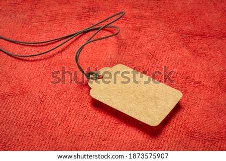 blank paper price tag with a twine against red textured handmade paper, shopping concept