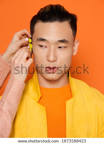 A man with an earring on his ear orange background and a yellow jacket