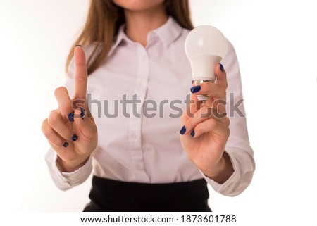 Brunette with a light bulb in her hands stands on a white background. Girl with a lamp in hand as a business idea. 