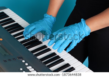 close-up of female hands and fingers in rubber medical gloves playing a melody on an electronic synthesizer, side view isolated on a blue background.