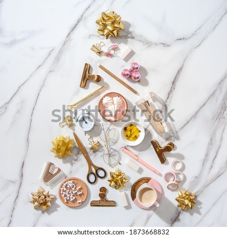 Top view of creative Christmas tree shape made of office stationery, alarm clock, Christmas decoration elements and coffee with marshmallow with copy space on white marble background. Festive holidays