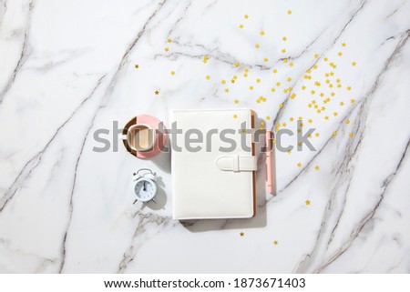 Notebook with empty pages for your text, pen, coffee cup, milk, small gift boxes with pink ribbon and golden sparkles on white marble table. New Year and Christmas concept, top view. Festive holidays