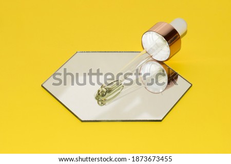 pipette dropper with retinol beauty oil on a mirror hexagon on illuminating yellow background with focus on pipette