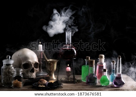 Magic and wizardry concept. Magic potions, skull,books and candles on table. Potion with vapor streaming from bottle.  Witch's house. Royalty-Free Stock Photo #1873676581