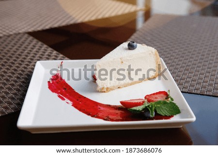 White Slice of cake with fresh grape berries lying on a plate with strawberries. Selective focus.