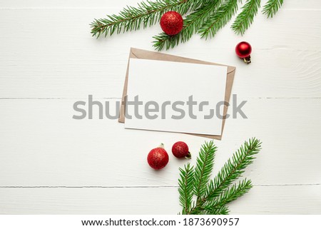 Greeting card mockup with red christmas decorations and fir tree branches on white wooden background