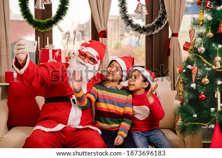 Santa sitting on sofa taking selfie with kids on Christmas