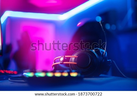 Professional headphones with microphone for video games and cyber sports gaming monitor in neon color blur background.